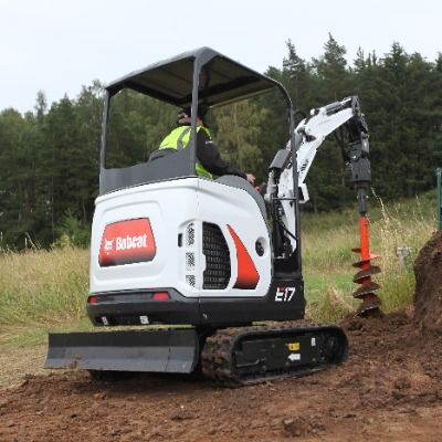 Baugeräte und Baustellenbedarf mieten - Weisser Minibagger von der Marke Bobcat bohr mit einem roten Bohraufsatz ein Loch in den Erdboden