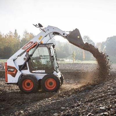 Baugeräte und Baustellenbedarf mieten - Weisser Lader von der Marke Bobcat kippt Erde auf den Boden aus