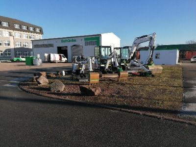 Baugeräte und Baustellenbedarf mieten - Weisse Lagerhalle mit geparkten Baggern auf dem Parkplatz vor der Halle