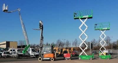 Baugeräte und Baustellenbedarf mieten - Zwei grüne Scherenarbeitsbühnen und ein orangener Gabelstapler stehen auf einem Parkplatz